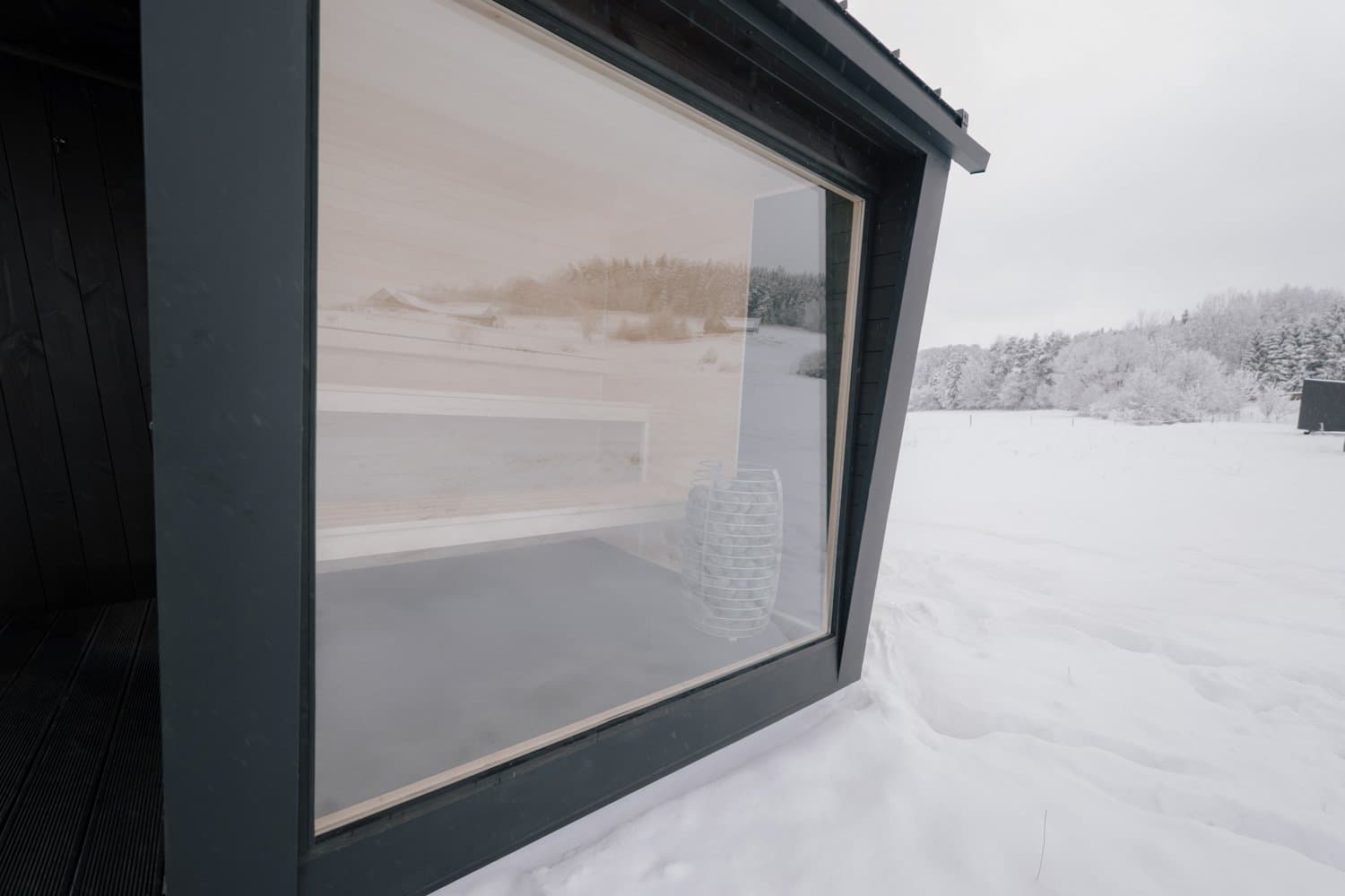 Das Eckfenster der Sauna Ikigai 5 von außen, Espenbänke und HUUM Ofen durch das Glas sichtbar