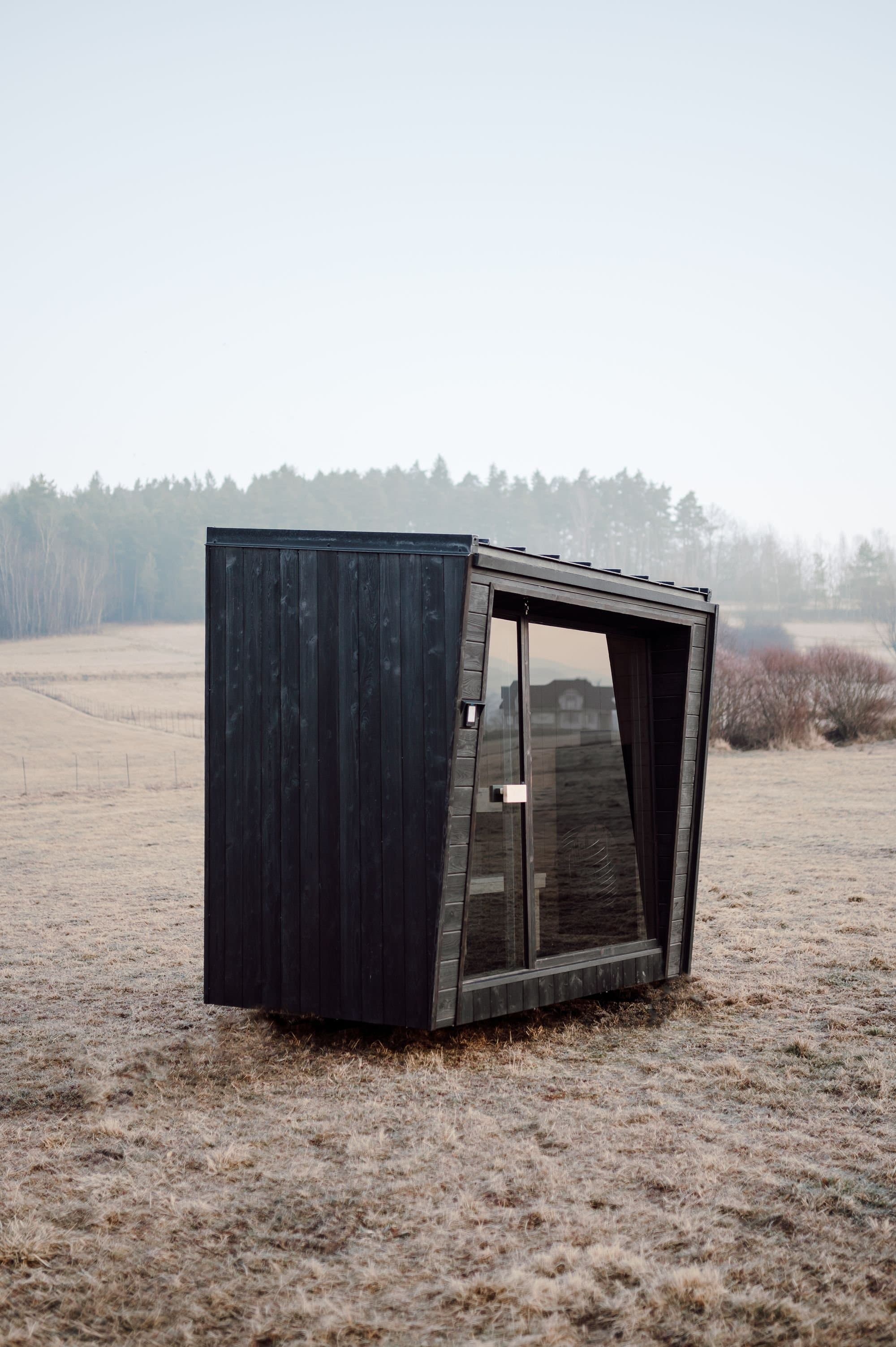 Seitenansicht der Sauna Kaizen mit verkohlter Verkleidung und Glasfront auf einem nebligen Winterfeld