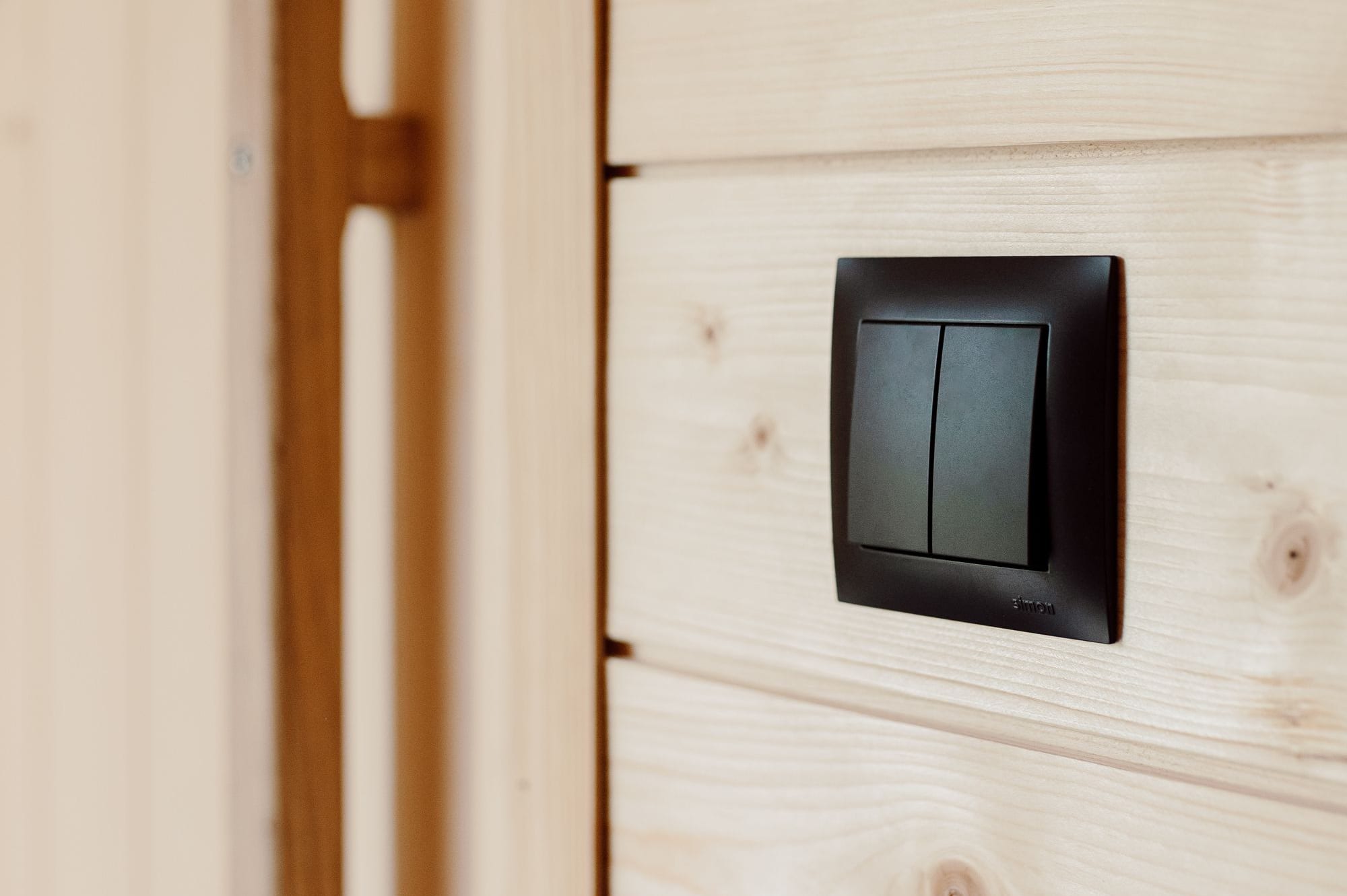 Schwarzer Lichtschalter auf heller Innenverkleidung neben der Tür einer Yuki Sauna Hansei