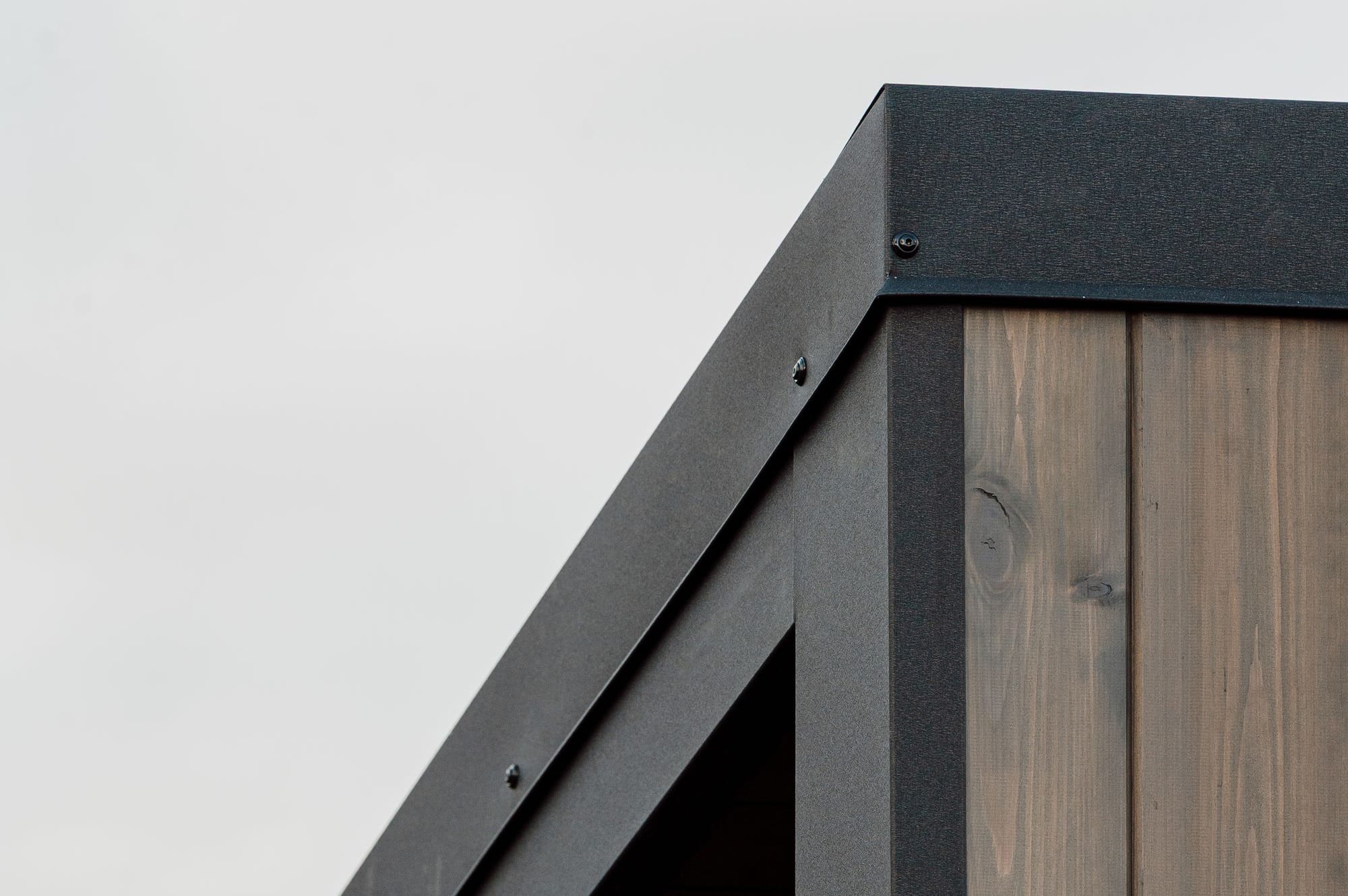 Dachkante einer Yuki Sauna Hansei, an der die schwarze Metallabdeckung auf die senkrechte Fassade aus thermisch modifizierter Kiefer trifft