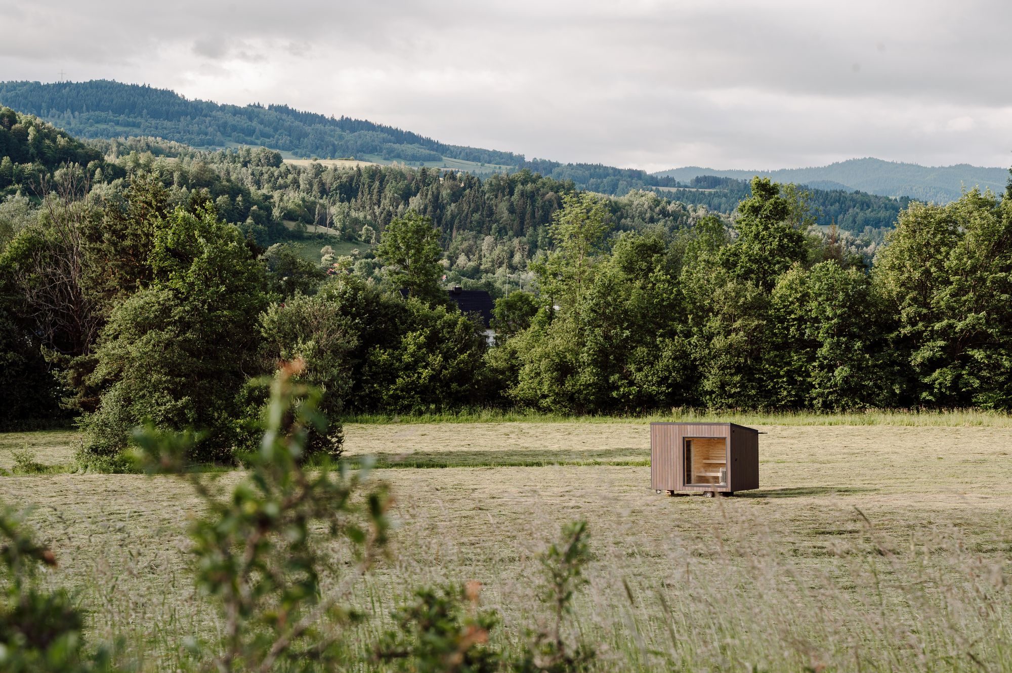 Sauna Hansei na łące, w tle zalesione grzbiety Beskidów
