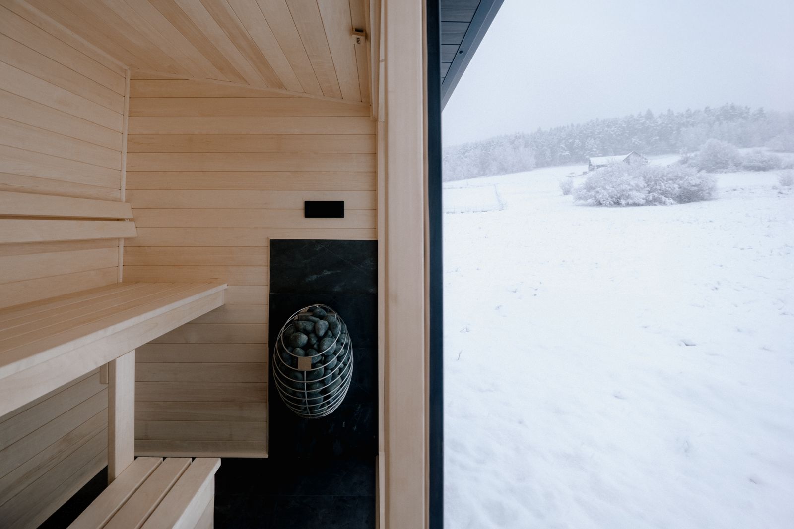 Sauna Kaizen interior showing heater, ventilation grille and panoramic window with winter view