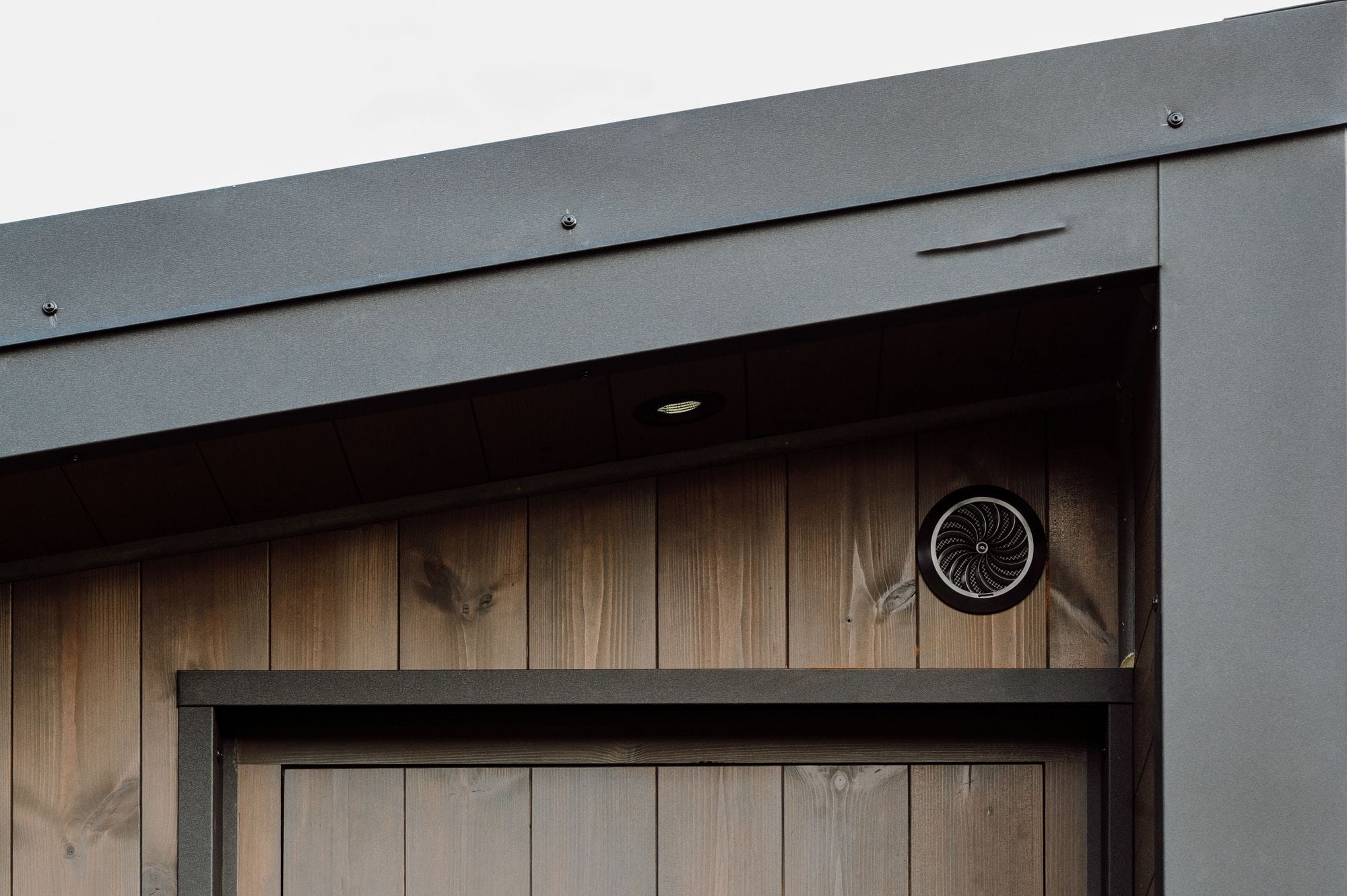 Ronde ventilatie-inlaat in thermogrenen gevelbekleding boven een saunadeur